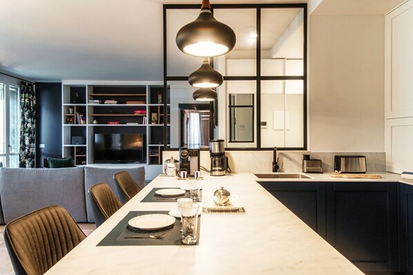 A modern kitchen with a dining area, a coffee maker, and a TV in the background. - Blue Stay - My Home in Como (Riva)