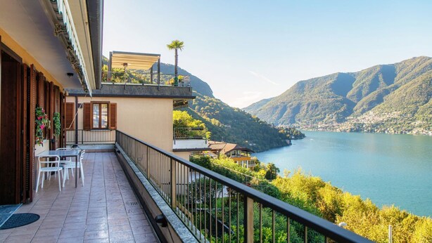 A balcony with a view of a lake and mountains, a table with chairs, and a small garden area. - Blue Stay - My Home in Como (Riva)