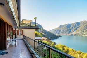 A balcony with a view of a lake and mountains, a table with chairs, and a small garden area. - Blue Stay - My Home in Como (Riva)