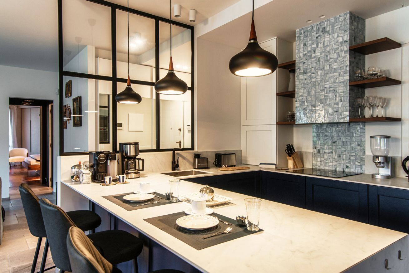 Une cuisine moderne dotée d’un îlot central, de luminaires suspendus et d’un revêtement mural décoratif à motifs géométriques.