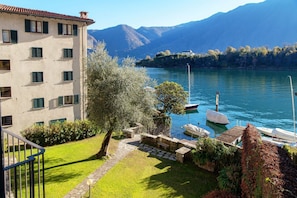 Un edificio con una terrazza che si affaccia su un lago, barche ormeggiate e montagne sullo sfondo.