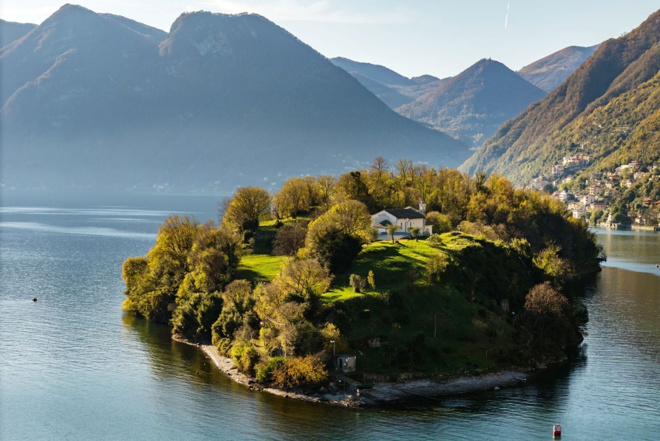 A small island with a house surrounded by trees and a lake.