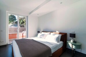 A bedroom with a bed, a nightstand, a window with a view of a balcony, and a door.
