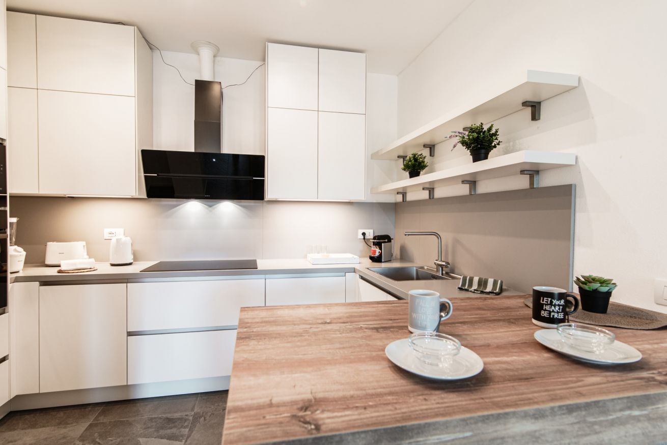 Una cucina moderna con mobili bianchi, un tavolo da pranzo in legno e una macchina da caffè.