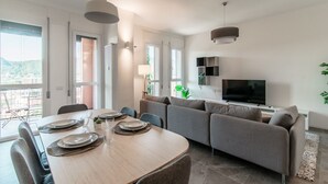 A modern living room with a dining area, a sofa, a TV, and a balcony with a view. - Friends & Family Retreat - My Home In Como (Como)
