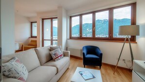 Un salon comprenant un canapé, un fauteuil, une table basse, une lampe et de grandes fenêtres donnant sur une vue sur la montagne.