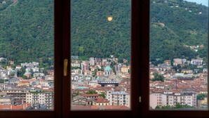 Une vue sur la ville à travers une fenêtre, avec des bâtiments, un dôme verdâtre et une colline en arrière-plan.