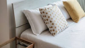 Un lit avec une literie blanche, une tête de lit en bois et deux oreillers à motifs à pois.