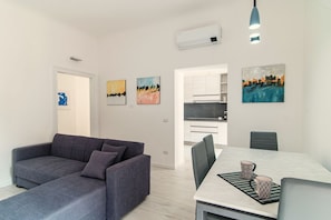 A modern living room with a grey sofa, a dining table with two chairs, and artwork on the walls.