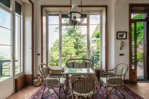 A dining area with wicker chairs, a glass table, and a view of greenery through large windows.