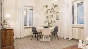 A dining area with a round table, four chairs, a vase with flowers, a wooden cabinet, and a large plant. - Wonder View - My Home In Como (Como)