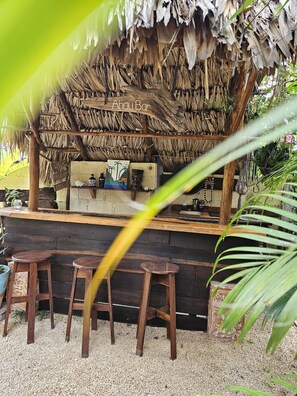 A rustic bar area with a thatched roof, wooden stools, and a concrete counter. - Jungla Bacalar (Bacalar)