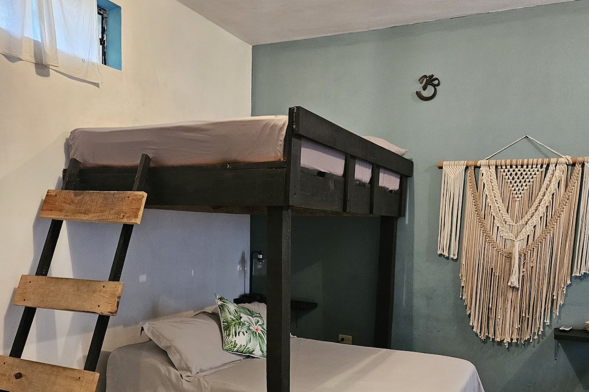 A bunk bed room with a ladder, a macrame wall hanging, and a small window.