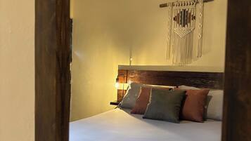 Un dormitorio con cama, aire acondicionado de pared, un colgador de macramé y cabecera de madera.