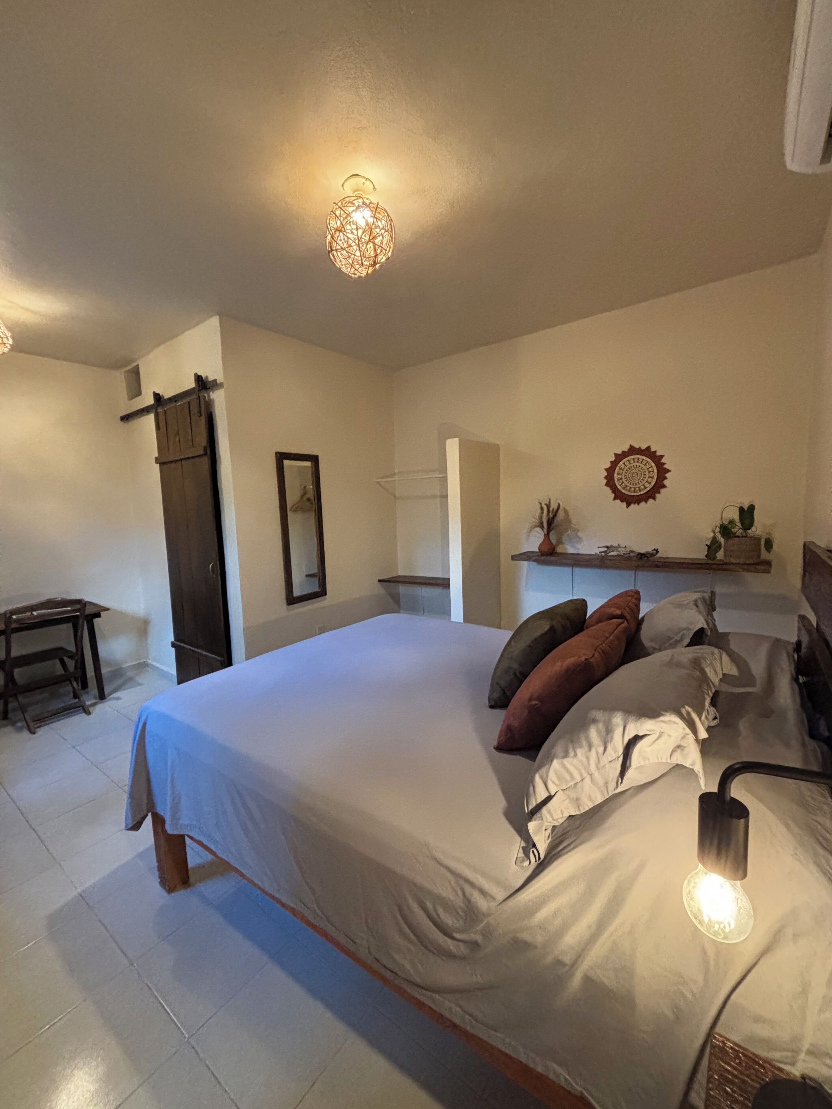 A bedroom with a bed, bedside lamps, a dresser, a mirror, and a shelf with decorative items.