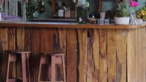 Una barra de madera rústica con taburetes, rodeada de follaje y macetas.