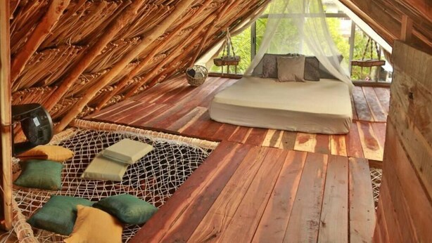 Una habitación acogedora con techo de madera, una cama, almohadas y un tapete tejido.