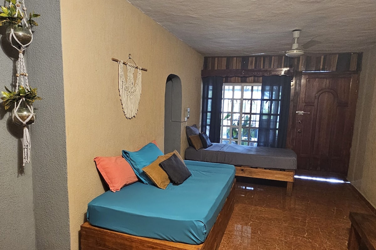 A bedroom with a bed, a wooden bench, a ceiling fan, and a window with curtains.
