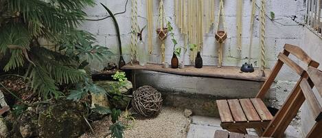 A rustic outdoor seating area with a wooden bench, a woven ball, and a wall adorned with macramé hangings and small potted plants.