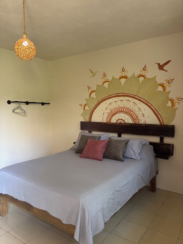 Un dormitorio con una cama, cabecera de madera, lámpara de pared y un mural decorativo.