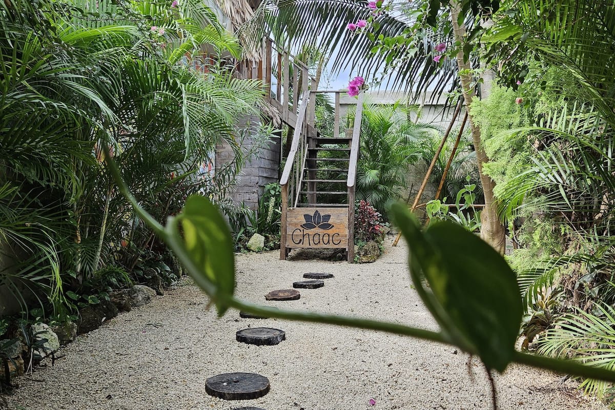 A garden pathway with a wooden sign reading "Chaac" leading to a staircase.