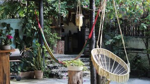Una silla hamaca, un taburete de madera y plantas en macetas en un entorno exterior.