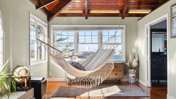A hammock in a room with large windows, a wooden ceiling, and a view of the city. - The widow’s walk your very own spa experience (Marblehead)