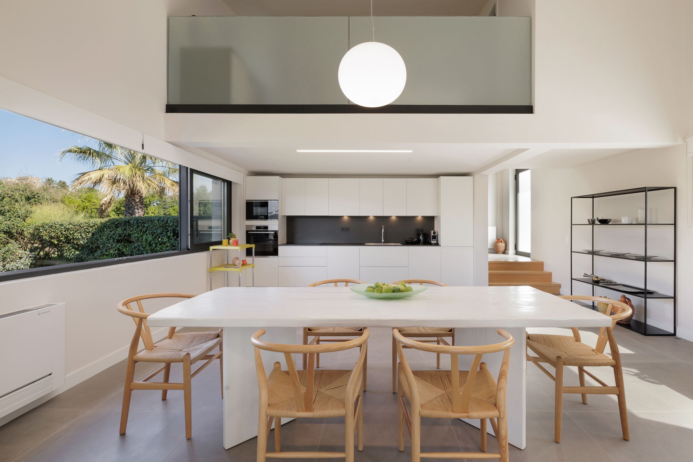 A modern kitchen with white cabinetry, a large island, and a dining area with six wooden chairs.