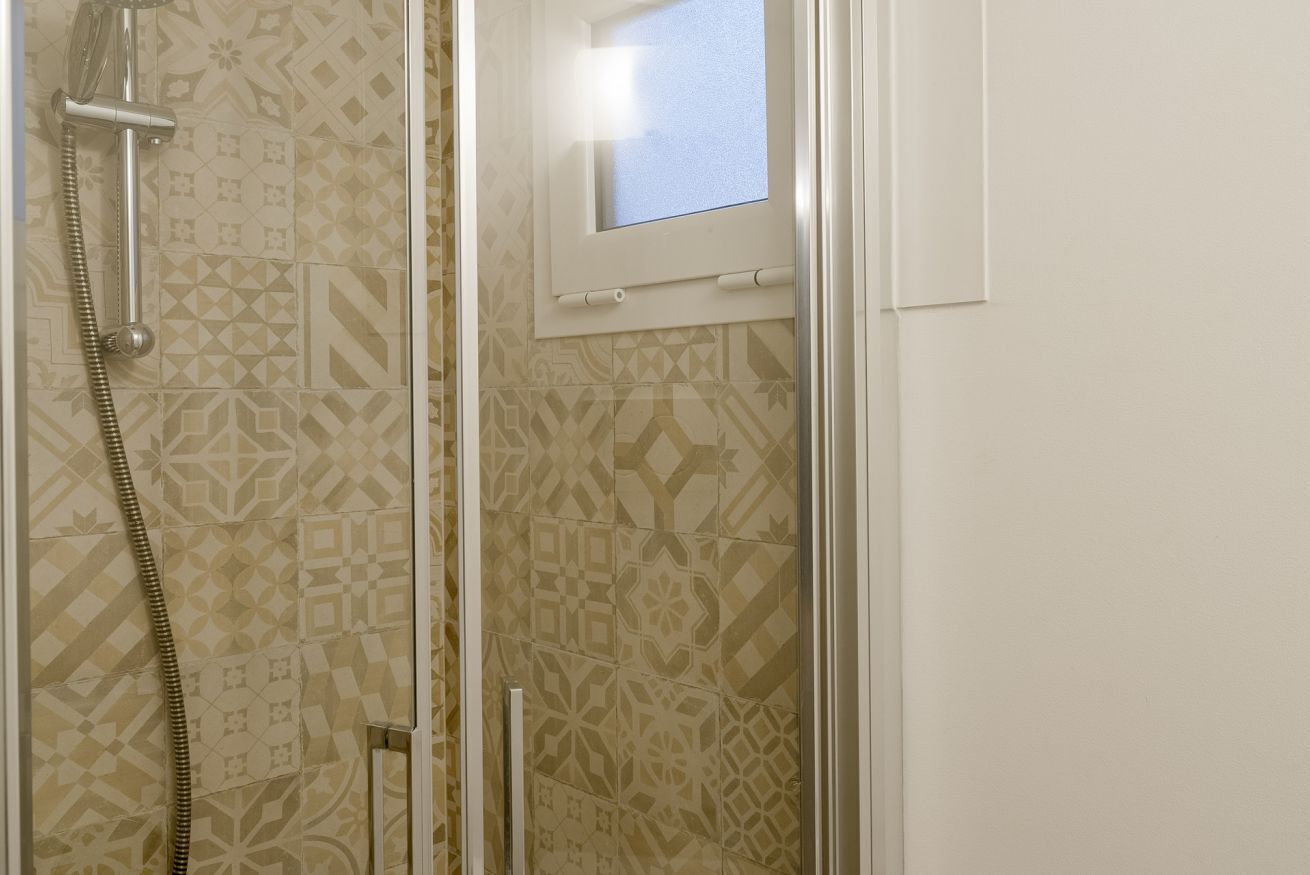 A shower with a glass door, patterned tiles, and a visible window.