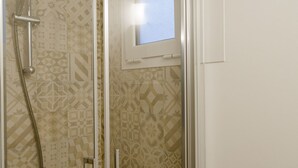 Ducha con puerta de vidrio, azulejos decorativos y ventana visible.