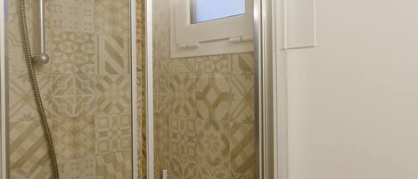 A shower with a glass door, patterned tiles, and a visible window.