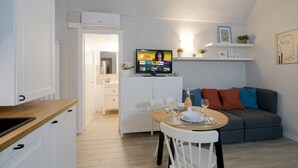Un espacio habitable compacto con kitchenette, zona de comedor, sofá y televisor montado en la pared.