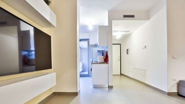 Un pasillo moderno con una televisión de pantalla plana, una zona de cocina y una puerta que da a otra habitación.