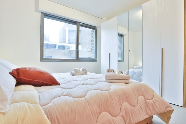 A bedroom with a bed, pillows, a window, and a wardrobe.