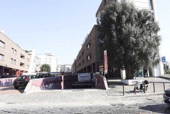 Vista de la calle con un edificio, coches aparcados y un árbol.