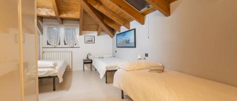 A bedroom with two single beds, a radiator, a window with curtains, a picture on the wall, and a wooden ceiling.