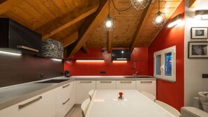 Een moderne keuken met witte kastjes, een rode accentmuur en een houten plafond.