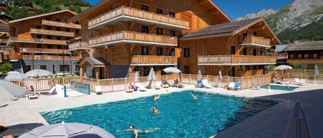 A wooden chalet-style hotel with a swimming pool, multiple balconies, and outdoor seating areas.