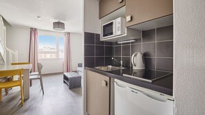 A modern kitchen with a built-in microwave, sink, and kettle. There is a dining area with a table and chairs visible.