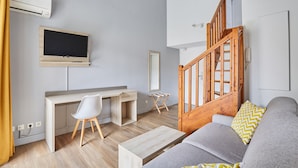 Ein modernes Wohnzimmer mit einem Holztisch, einem grauen Sofa, einer Holztreppe und einem an der Wand befestigten Fernseher.
