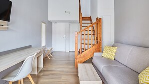 Ein modernes Wohnzimmer mit einer Holztreppe, einem grauen Sofa, einem Holztisch und einem flachbildfernseher, der an der Wand angebracht ist.