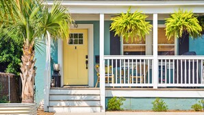 A house with a yellow door, white porch, and green plants. - Single Family Downtown House with Private Yard (Charleston)