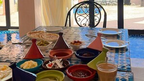 A dining table with various dishes and a view of a swimming pool and greenery. - Riad Timskrine  (Ourika)