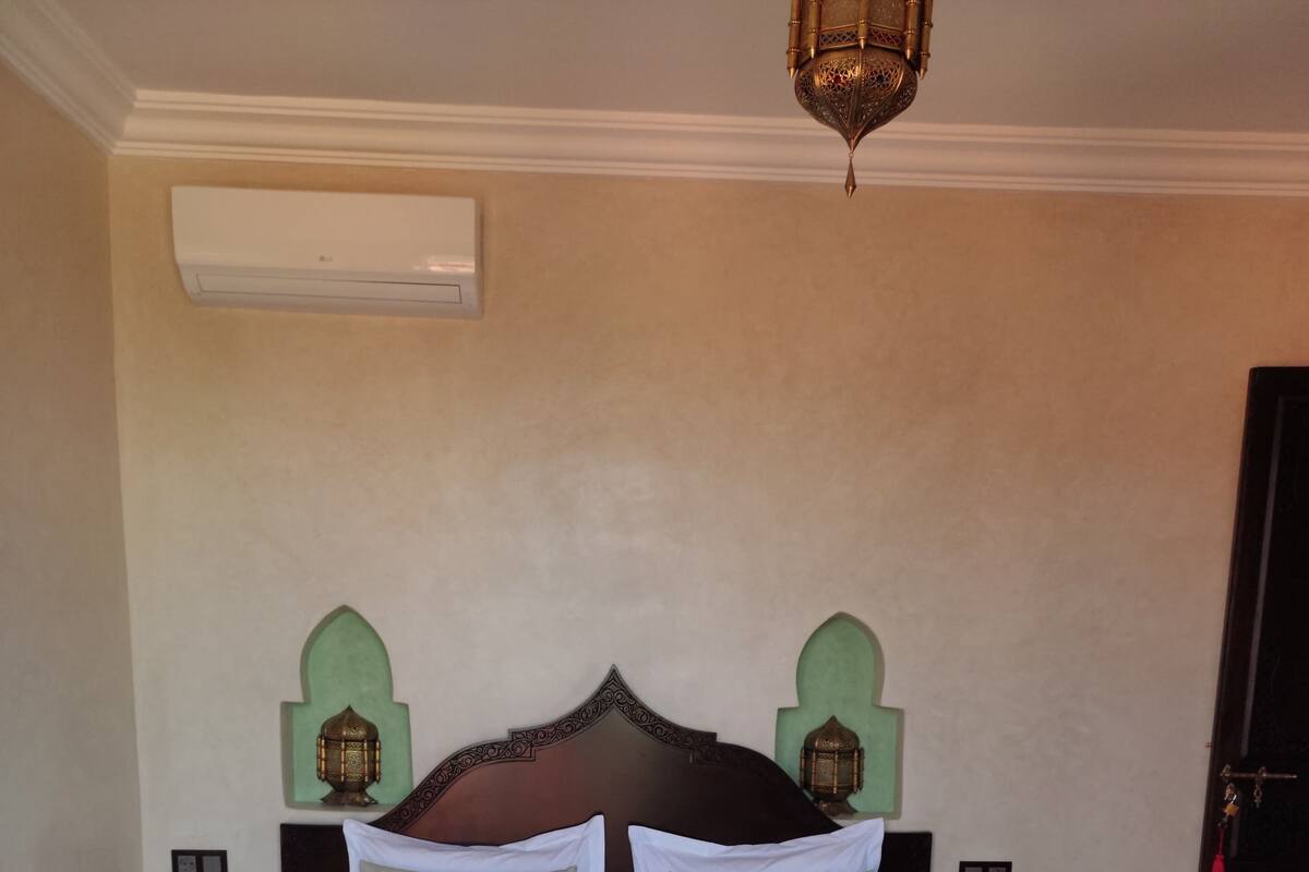 A bed with a wooden frame, green and white bedding, two nightstands with lamps, and a wall-mounted air conditioner.