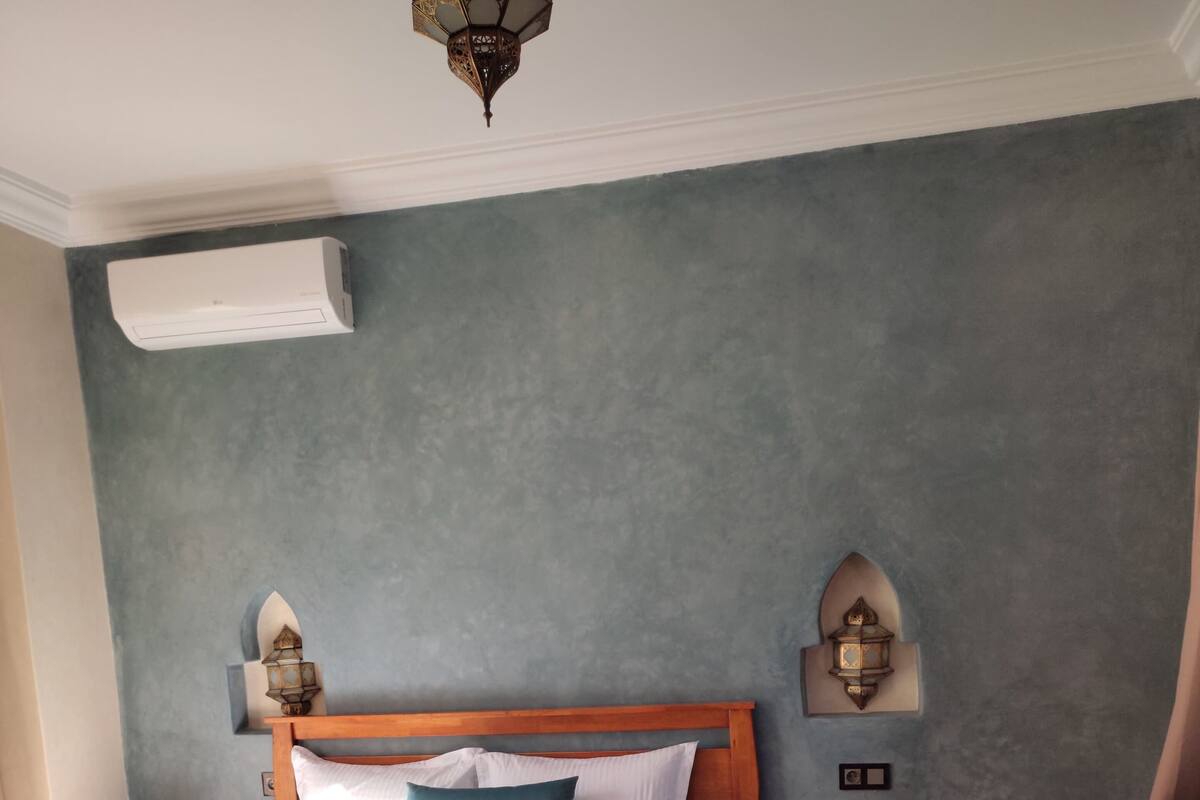 A bedroom with a wooden bed, bedside tables, a nightstand, a green sofa, and wall-mounted lamps.