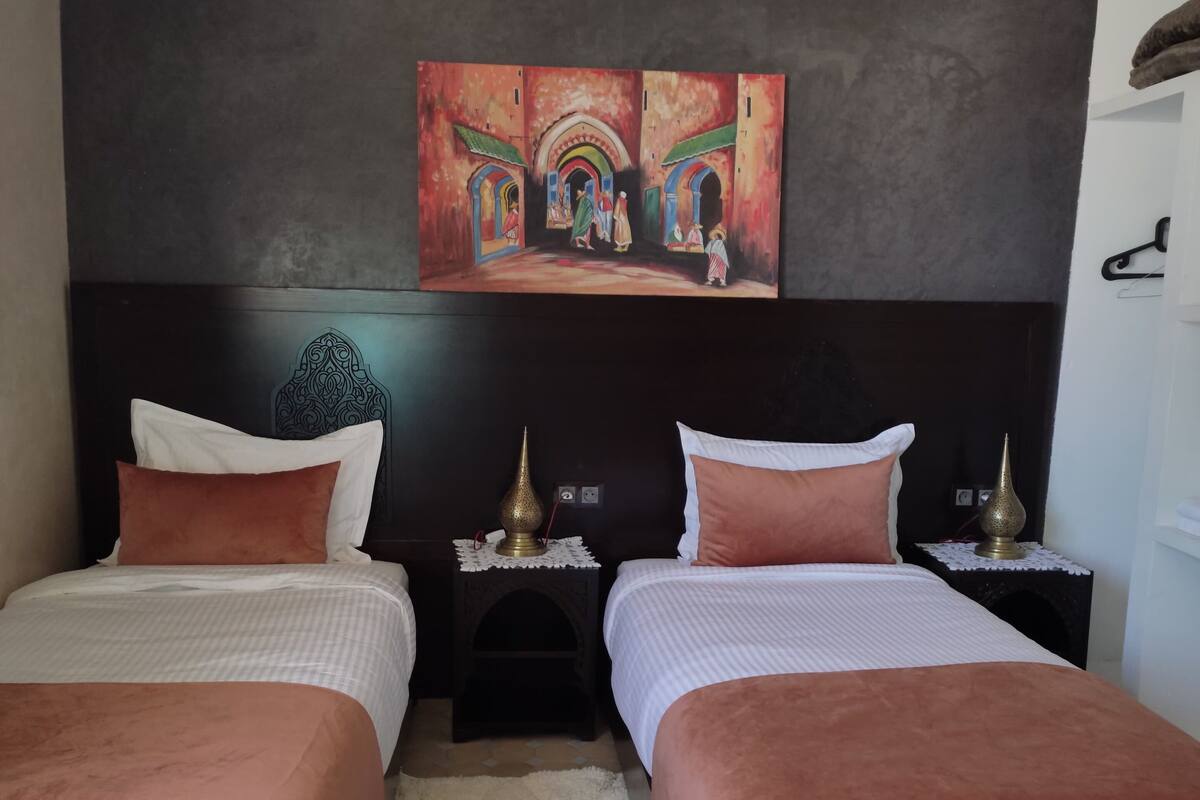 A hotel room with two beds, a dark headboard, a painting above the beds, and a small rug on the floor.