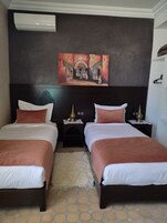 Habitación de hotel con dos camas, cabecero oscuro, un cuadro sobre las camas y una alfombra pequeña en el suelo.