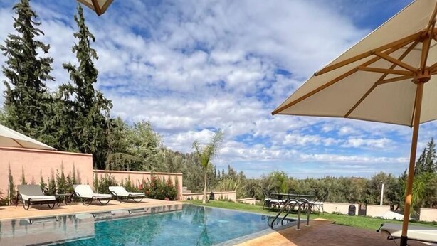 A swimming pool with lounge chairs and umbrellas, surrounded by a brick patio and greenery. - Riad Timskrine  (Ourika)
