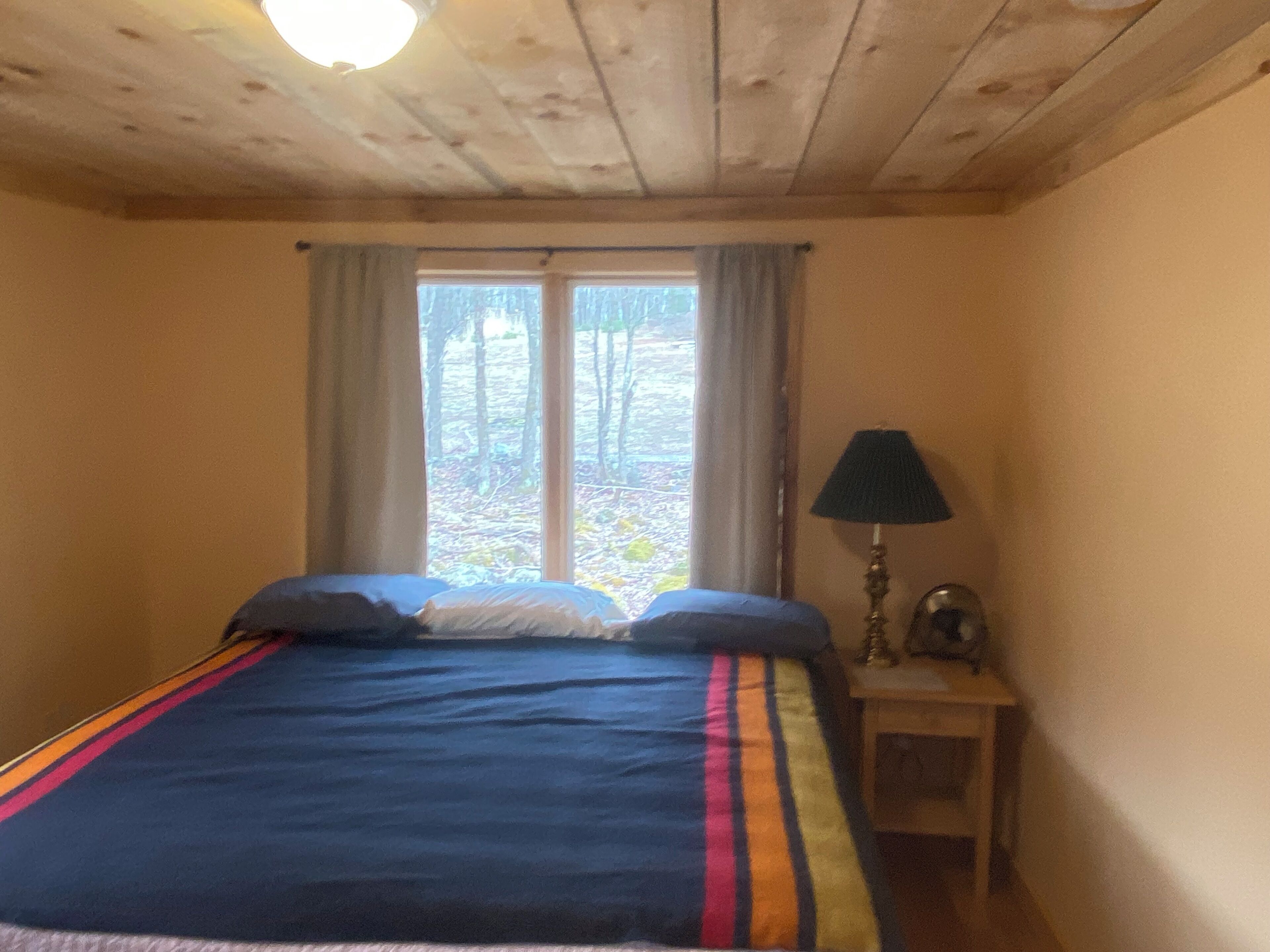 A bedroom with a bed, a window with curtains, a bedside lamp, and a small table.