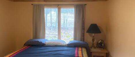 A bedroom with a bed, a window with curtains, a bedside lamp, and a small table.